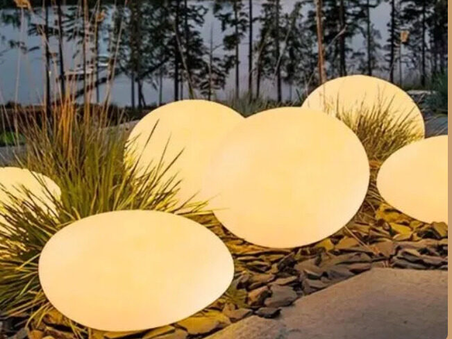 Soft glowing globe lights placed along a backyard lawn beside stones and tall grass at sunset