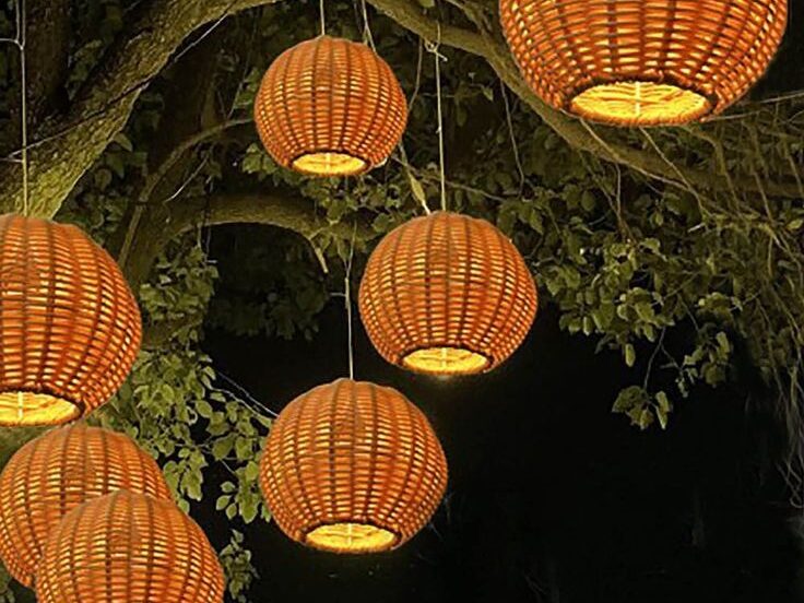 Warm woven lantern lights hanging from tree branches in a cozy backyard at night