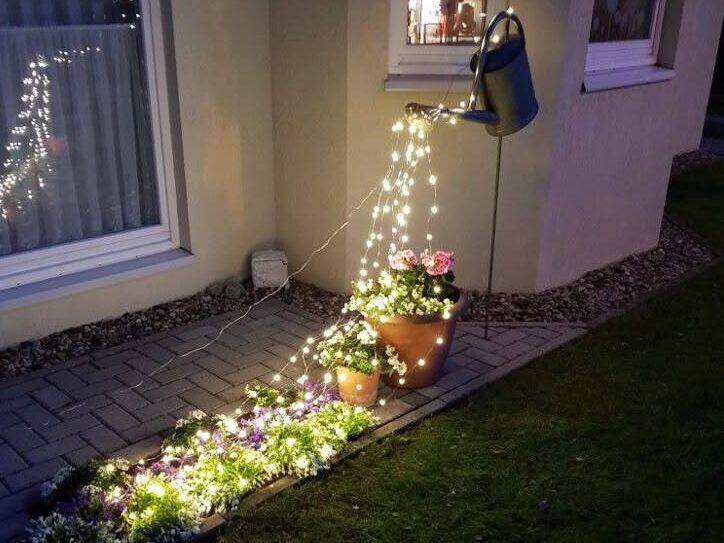 Tiny fairy lights flowing from a decorative watering can beside a porch wall at night